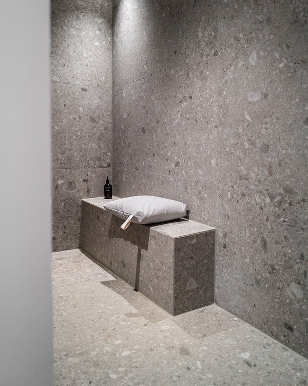 Frau sitzt entspannt auf einem Badesofa Sitzkissen (Farbe: Grau) auf einer gemauerten Bank in der Dusche.